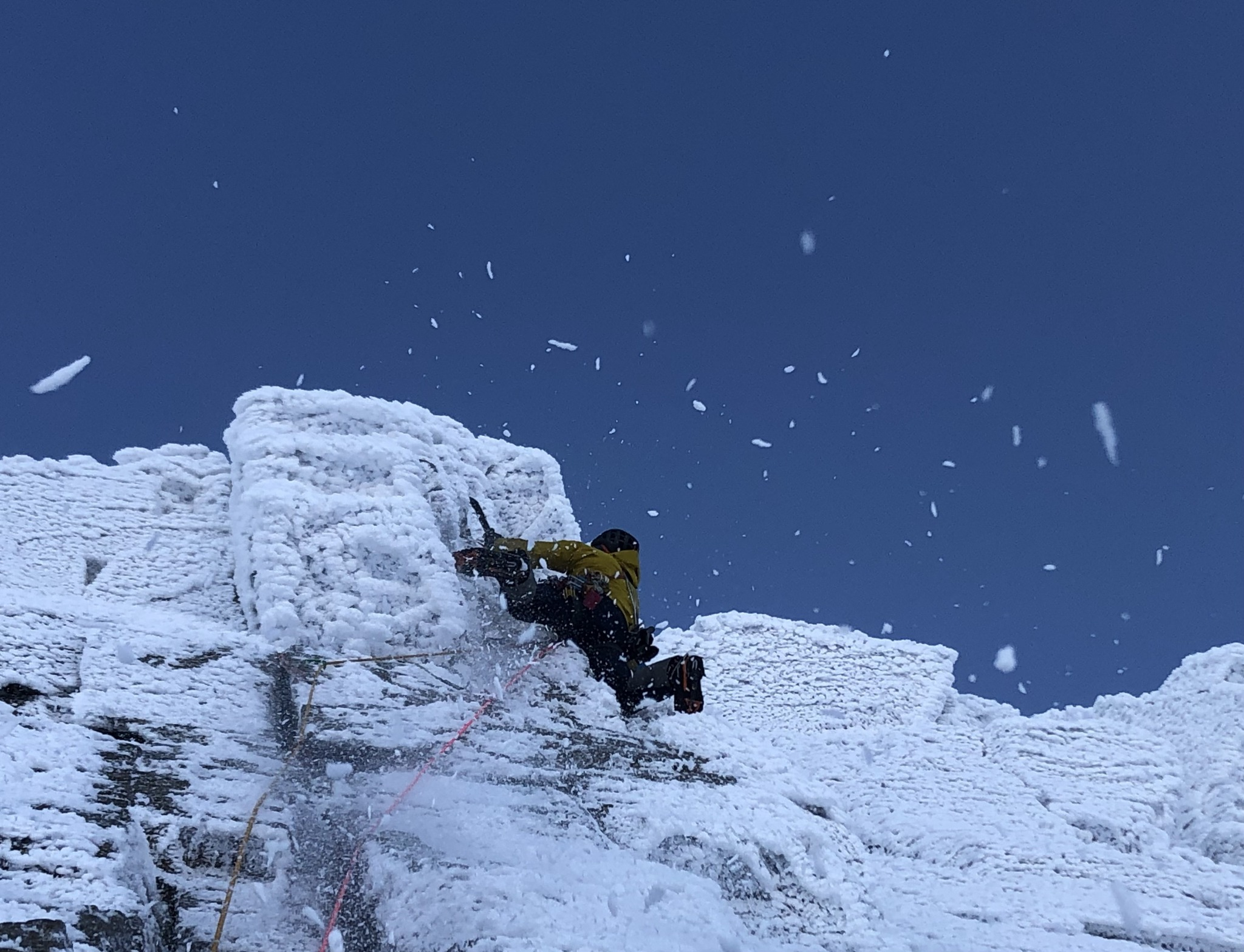 Winter climber on a steep snow-covered rock face with ice tools and rope