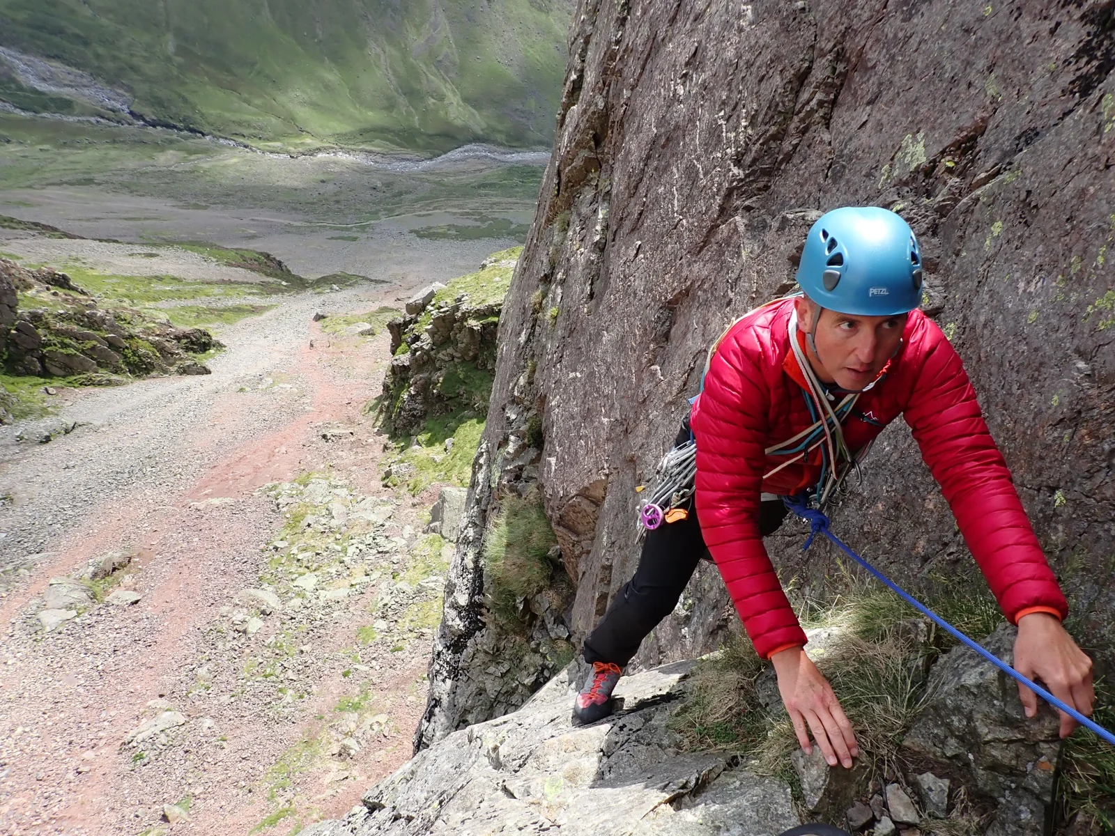 Climber in a blue helmet and red jacket ascending a rocky mountain route