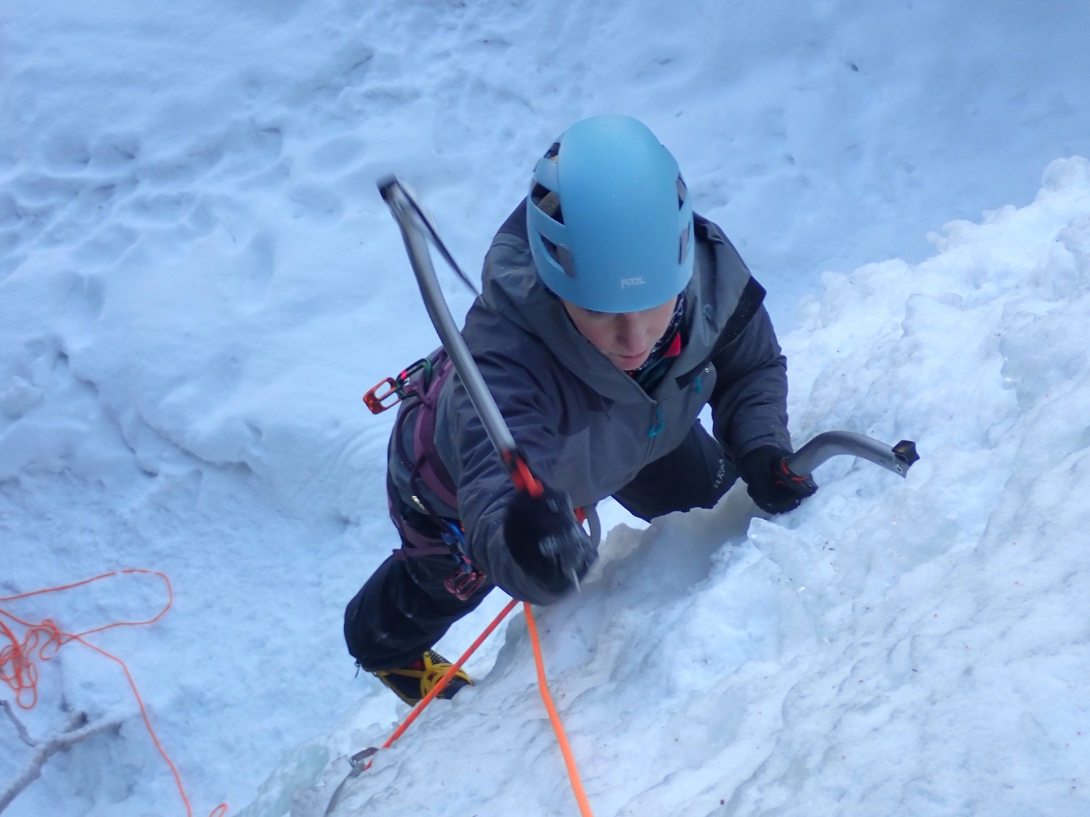 Ice climber with a blue helmet using ice tools on a frozen waterfall