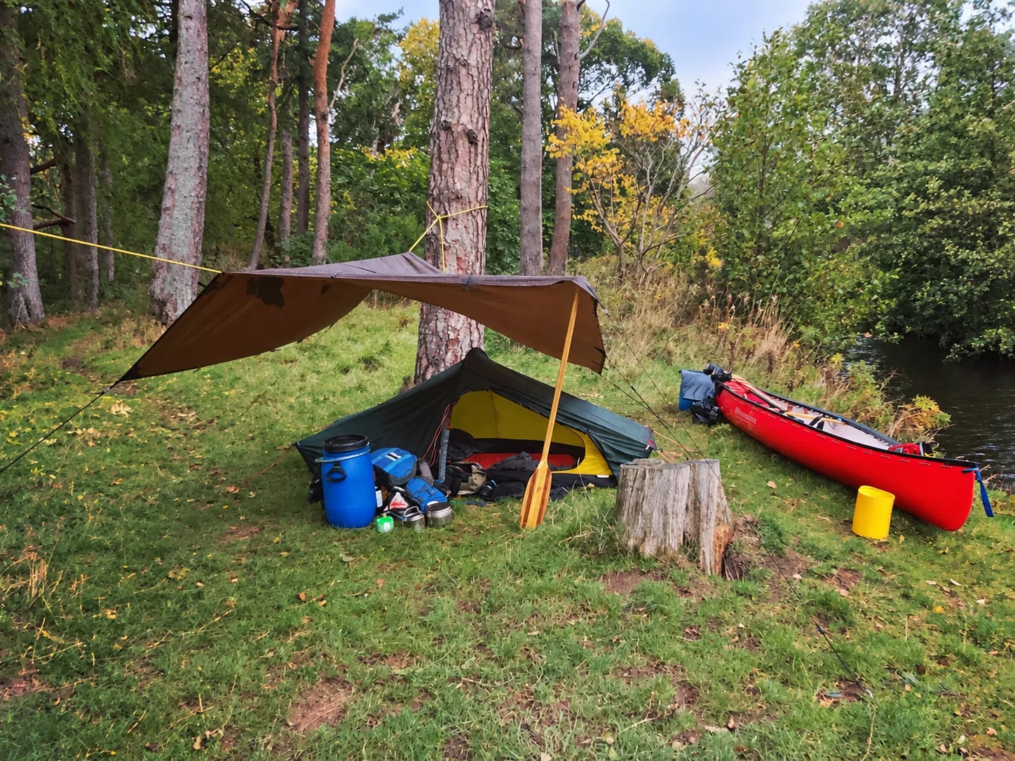 Woodland campsite with a tent, tarp and red open canoe