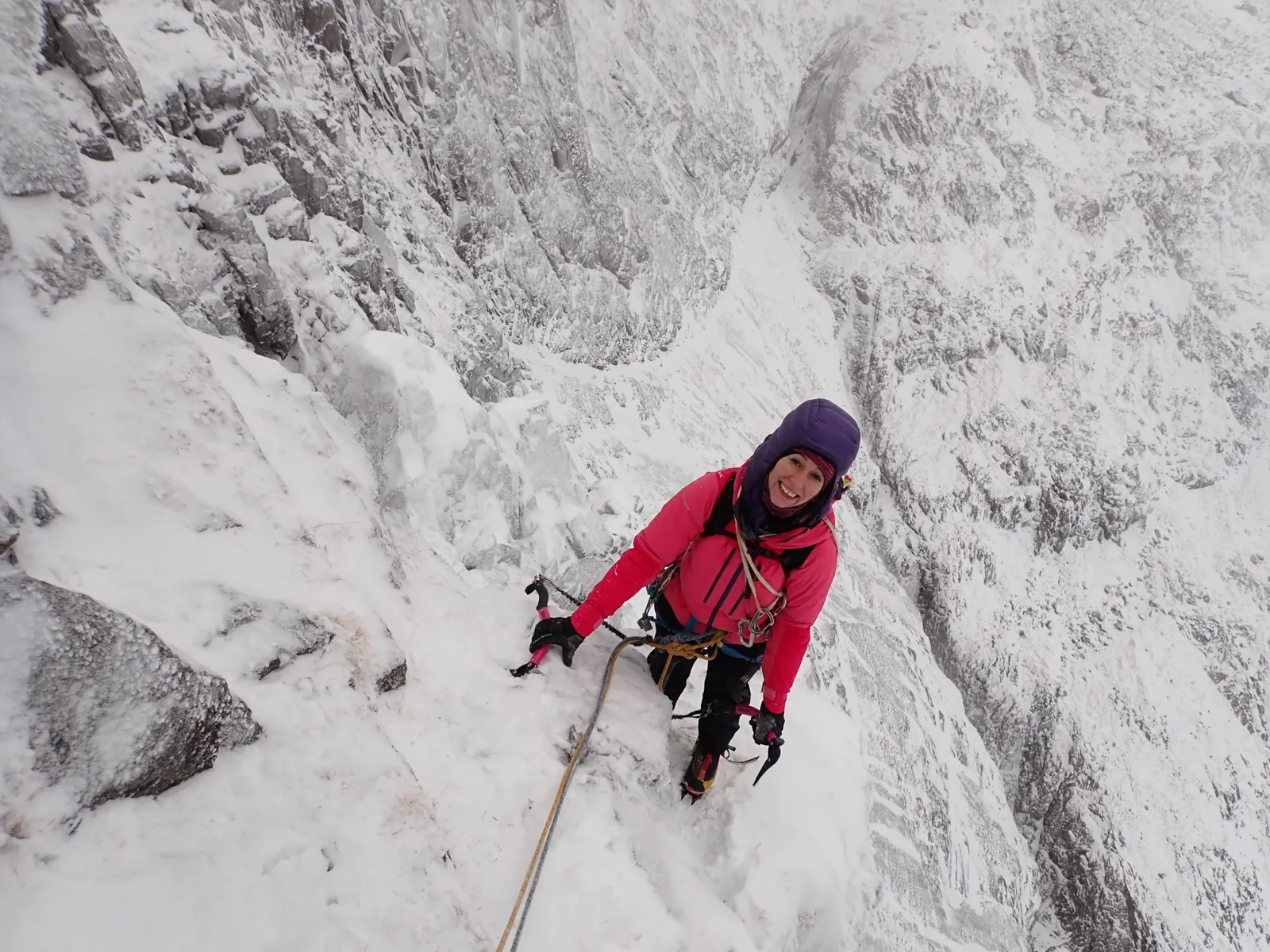 Winter climber with ice tools and ropes on a snowy mountain ledge
